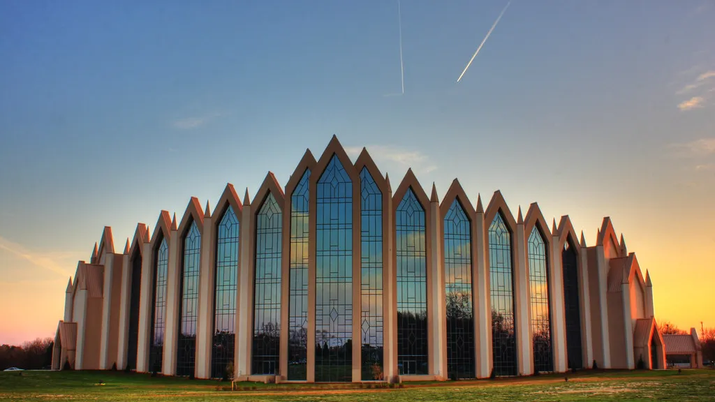 A modern church building with tall pointed glass facades seen from the lawn at sunset